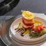 A plated gourmet dish featuring a stacked entrée with sauce