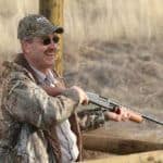 Person aiming a shotgun outdoors.